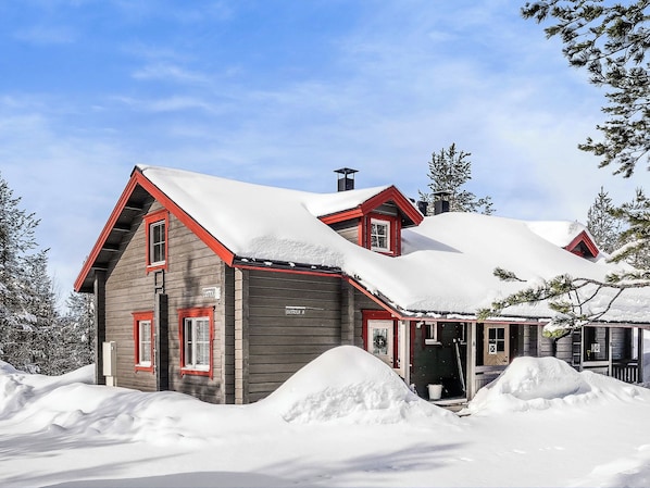 A two-story wooden house with a red roof and snow-covered surroundings.
