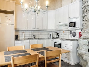 A kitchen with white cabinets, a chandelier, a microwave, and a dining area with wooden chairs and a table. - Lustola a by Interhome (Sodankylä)