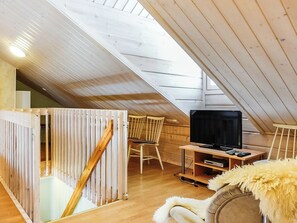 A high-ceilinged attic room with a wooden sloped roof, a television on a wooden stand, and a fluffy white throw on a chair. - Lustola a by Interhome (Sodankylä)