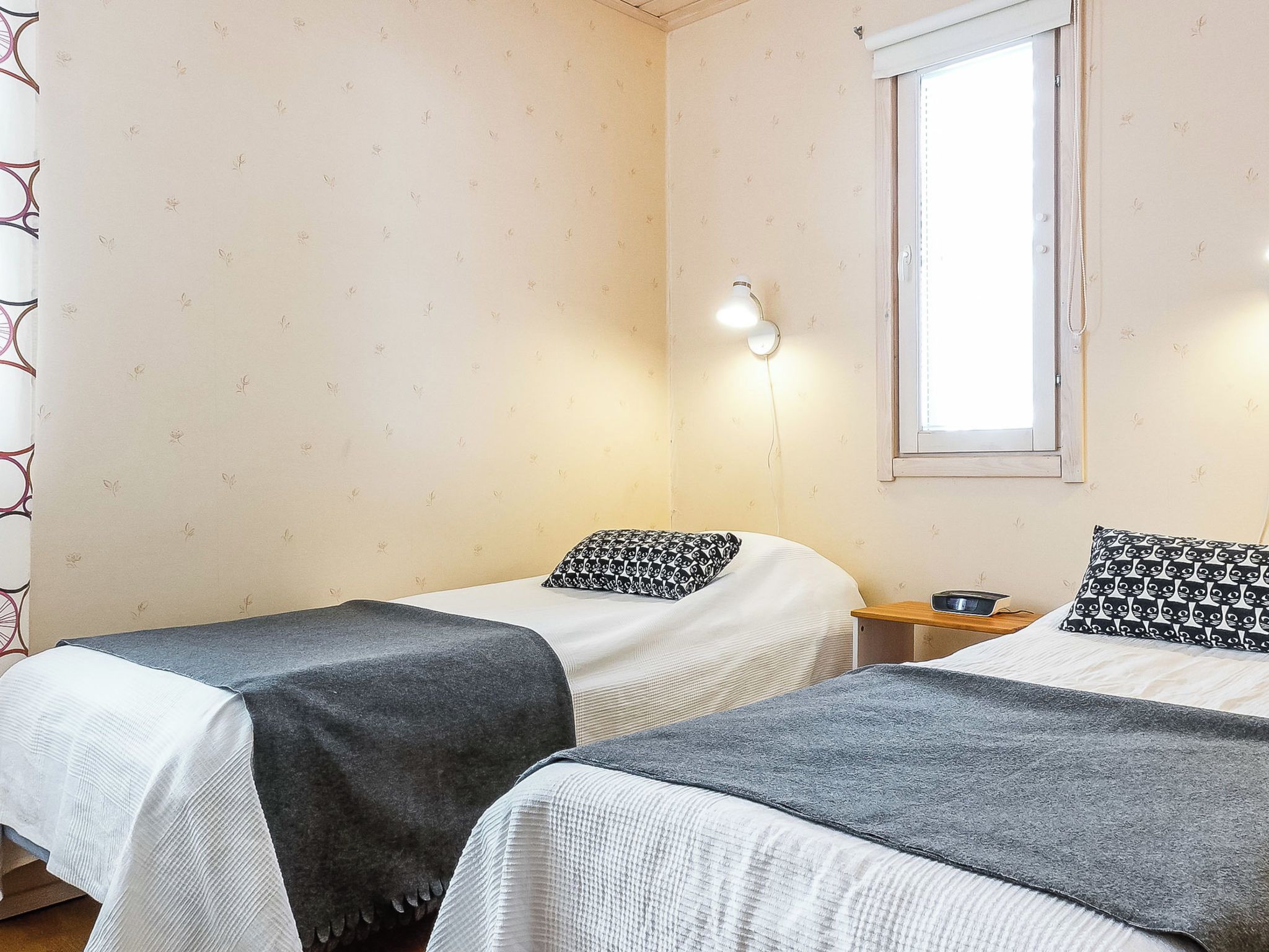Habitación doble con dos camas, una mesita de noche, una ventana y una lámpara de pared.