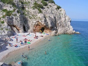 Ein Strand mit klarem türkisblauem Wasser, felsigen Klippen und Menschen, die sonnenbaden und schwimmen.