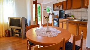 A compact kitchen with wooden cabinets, a stove, and a sink. There's a dining table with a lace tablecloth and chairs. - Apartment Zvonko by Interhome (Lovran)