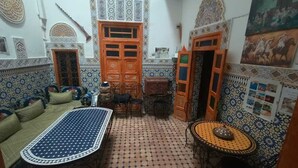 A traditional Moroccan interior with a patterned floor, a sofa, a dining table, and a decorative door. - Riad Drissia (Fes)