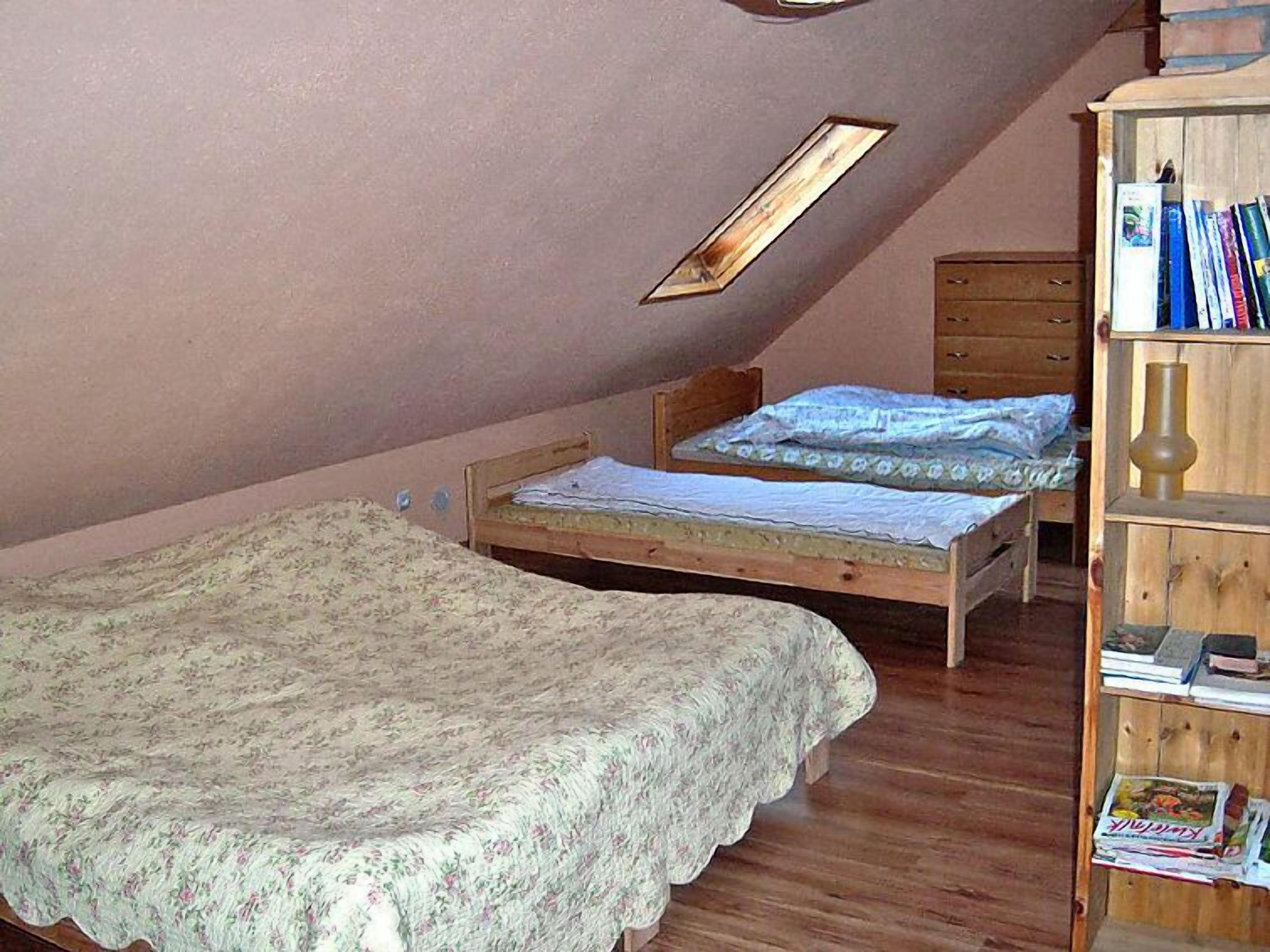 A small, cozy attic bedroom with two wooden beds, a wooden wardrobe, and a slanted ceiling.