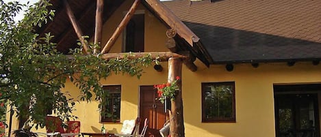 A rustic house with a stone wall, wooden porch, and a chimney.