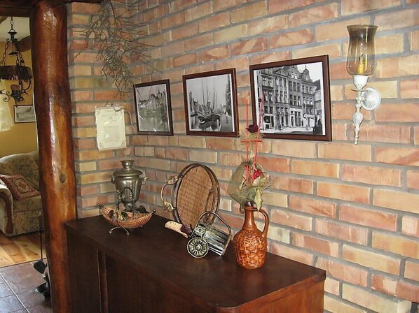 A room with a brick wall, a wooden table with vintage items, and framed pictures on the wall.