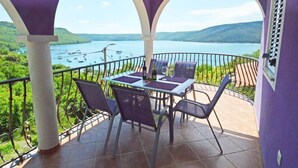 A balcony with a table and chairs, overlooking a lake with boats and hills. - Apartment Šverko by Interhome (Trget)