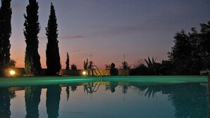 Ein klares Schwimmbecken mit Spiegelungen von Bäumen und einem Sonnenuntergang im Hintergrund.