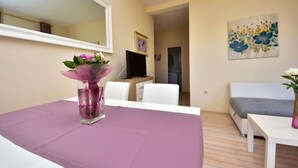 A modern living room with a white sofa, a small table, and a TV. There is a painting on the wall and a vase with flowers on the table. - Melandura by Interhome (Pag/Dinjiška)