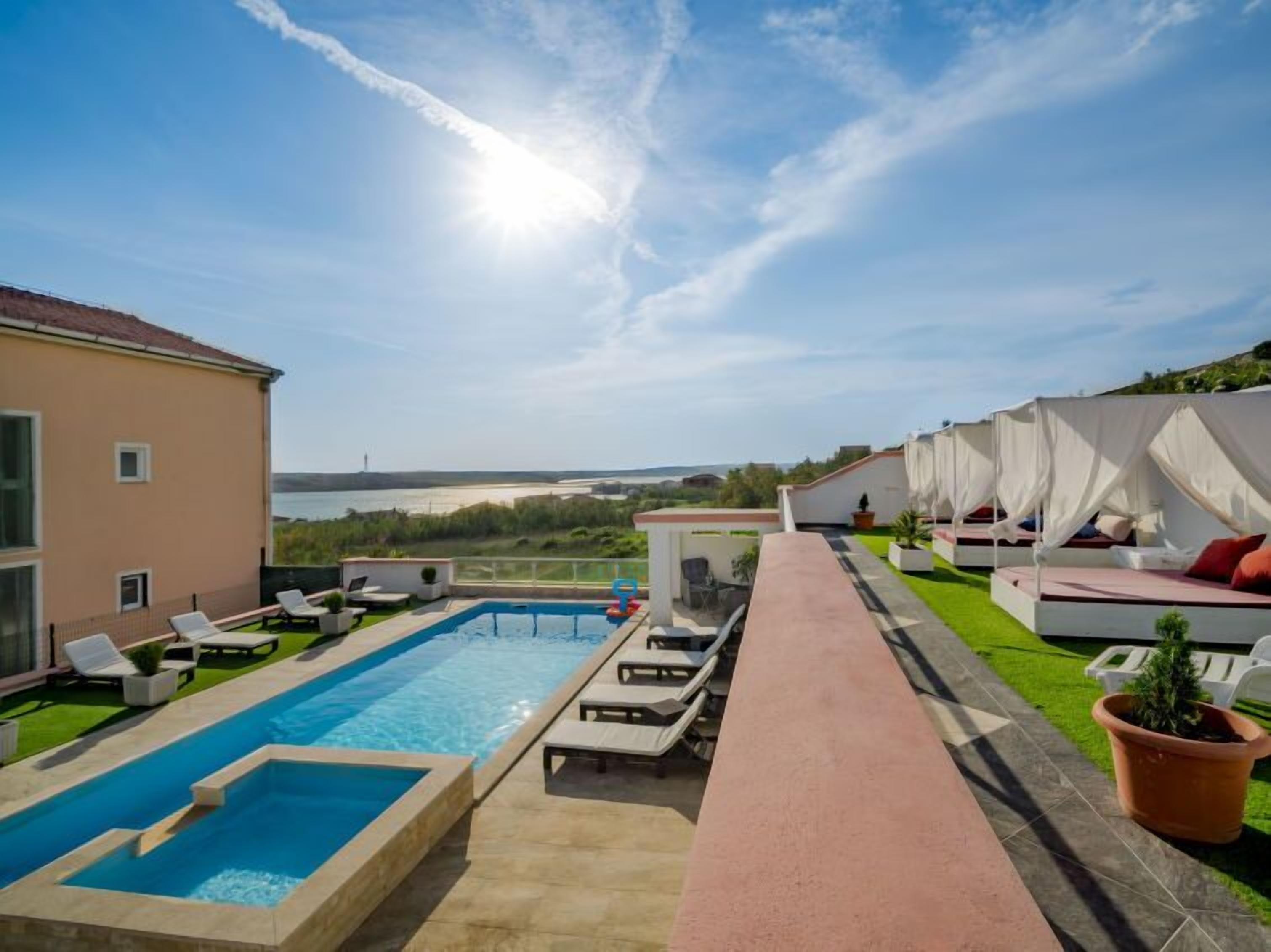 A rooftop pool area with lounge chairs, a swimming pool, and a view of the sea.