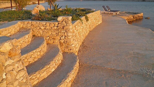 A stone pathway leading to a beach with lounge chairs and a thatched umbrella. - Melandura by Interhome (Pag/Dinjiška)