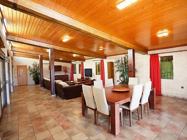 A spacious dining area with a wooden table and chairs, a sofa, and a television.