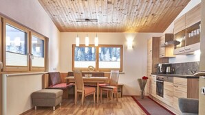 A modern kitchen with wooden cabinets, a dining area with a table and chairs, and large windows with a snowy view.