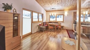 A modern interior with wooden flooring, a dining area, a kitchen, and large windows with a snowy view.