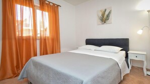 Un dormitorio con cama, cortinas, una mesita de noche, lámpara y una obra de arte en la pared.