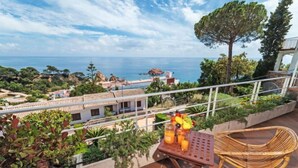 A balcony with wicker chairs, a table with fruit and drinks, and a view of the sea and buildings. - Vacation home Zen by Interhome (Tossa de Mar)