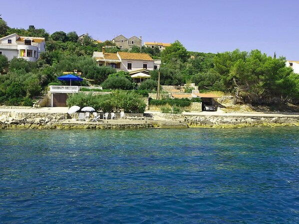A coastal property with a stone wall, a small pool, and several houses with red-tiled roofs.