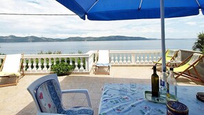 Une terrasse avec une table, des chaises et un parasol, d’où l’on peut admirer un plan d’eau et des montagnes lointaines.