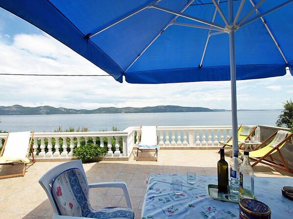 Een terras met tafel, stoelen en parasol met uitzicht op een wateroppervlak en verre bergen.