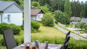 Ulkokäyttöön tarkoitettu ruokapöytä ja -tuolit on asetettu paikkaan, josta avautuu näkymä asuinalueelle, johon kuuluu taloja ja viheralueita.