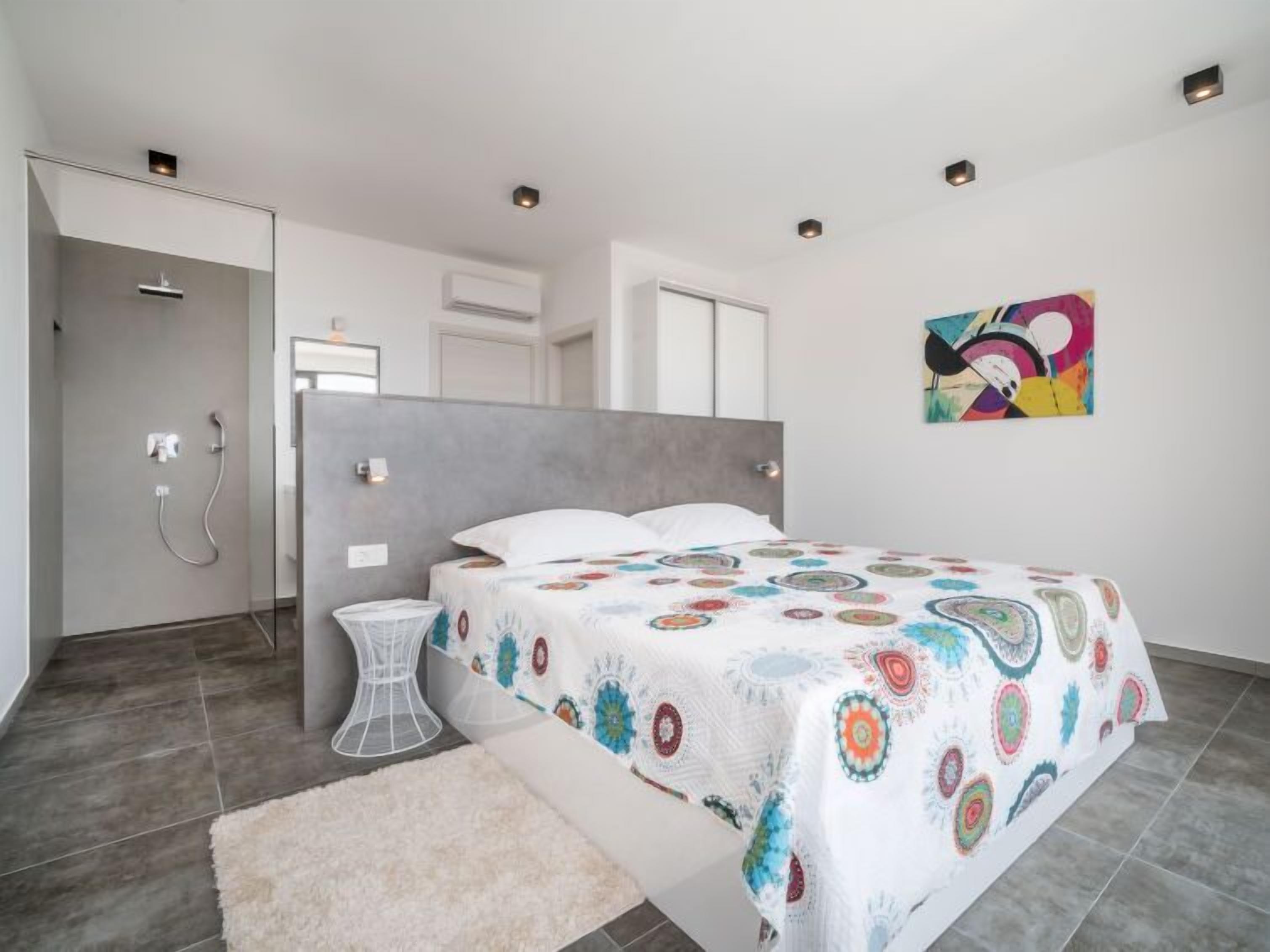 A modern bedroom with a large bed, a shower area, and a colorful abstract painting on the wall.