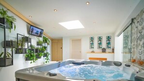 Ein modernes Badezimmer mit einer großen Whirlwanne, einem an der Wand montierten Fernseher und mehreren Blumentöpfen.
