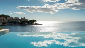 An infinity pool with a clear view of the sea and a coastal town in the background.