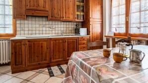 A kitchen with wooden cabinets, a tiled backsplash, a sink, a microwave, and a table with a tablecloth. - Hérisson by Interhome (Sarre)