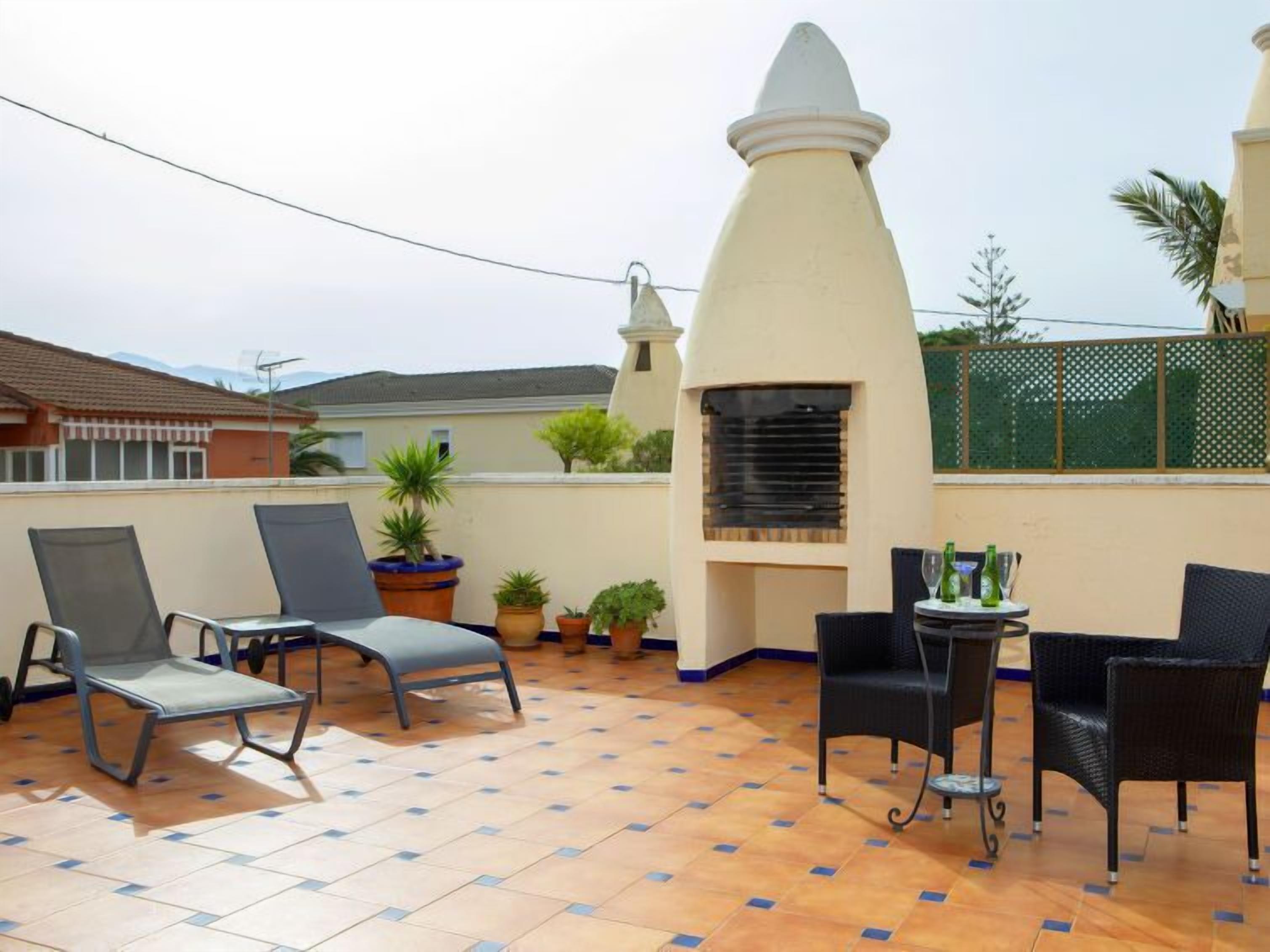 A rooftop patio with outdoor seating, a grill, and potted plants.
