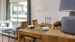 Un comedor con una mesa de madera preparada para el desayuno, un sofá y una ventana con cortinas.