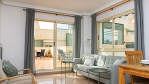 Una sala de estar moderna con un sofá, una mesa de comedor y una silla. Hay un ventanal corredero que da a un patio exterior.