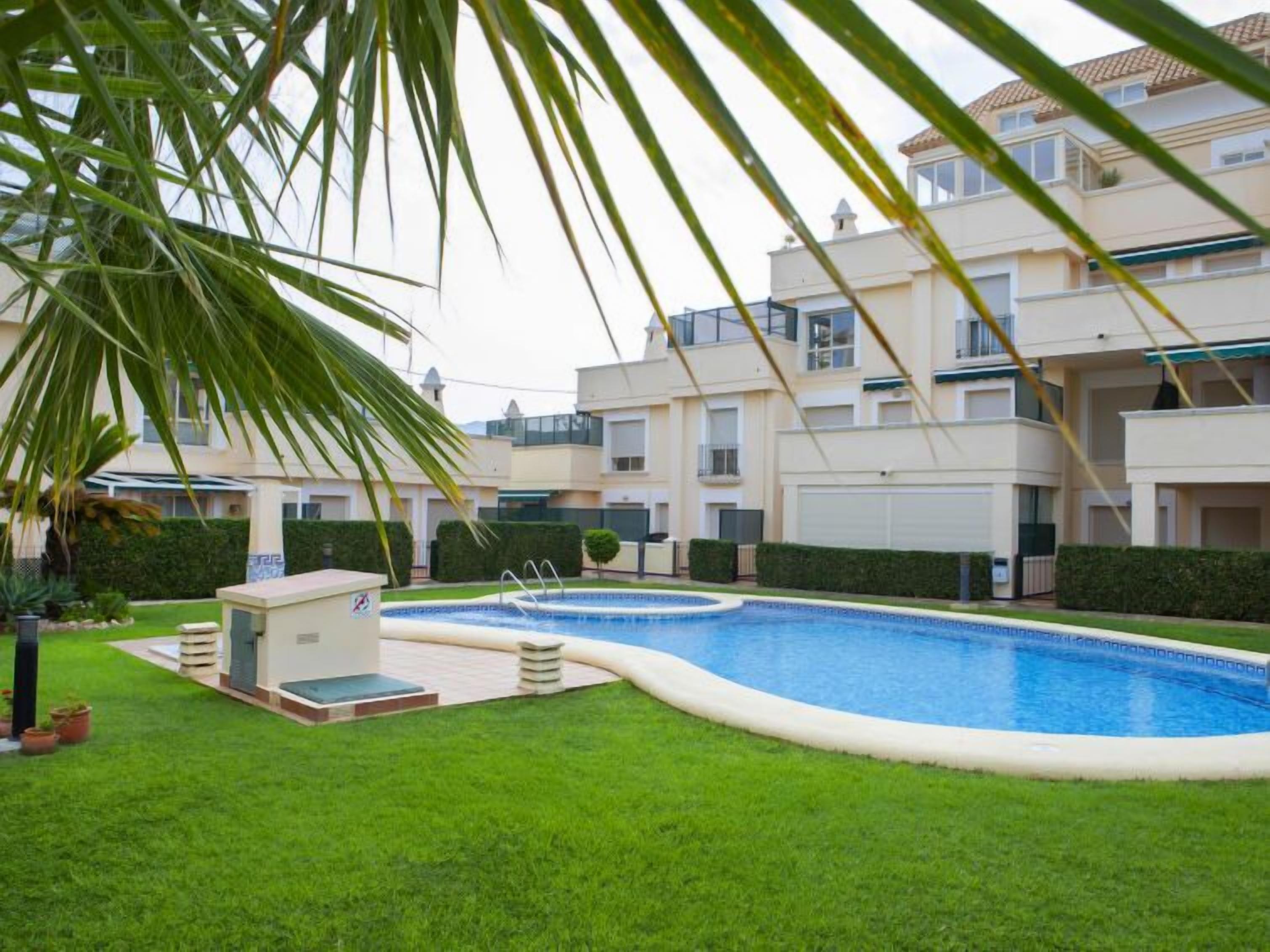 A residential building with a swimming pool, a small outdoor seating area, and well-maintained greenery.