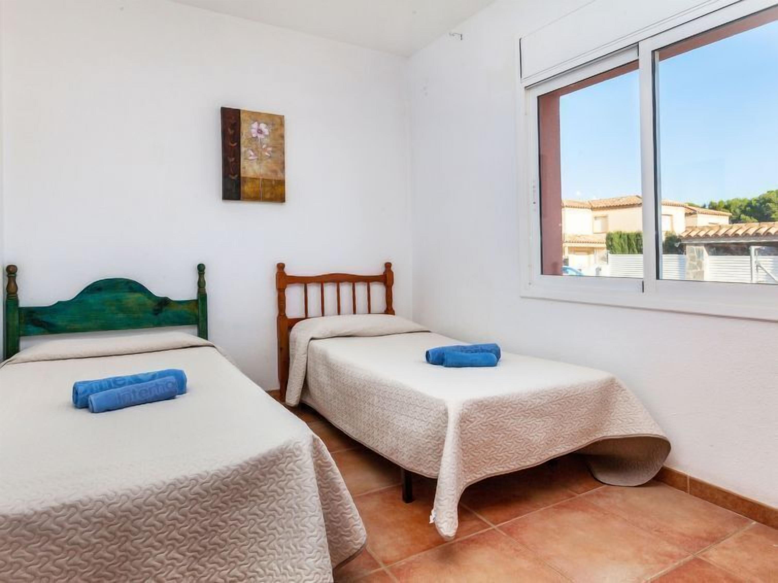 A small room with two single beds, a window, and a painting on the wall.