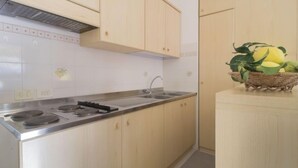 A kitchen with light wooden cabinets, a stainless steel sink, and a stove. There is a basket with lemons on a small table.