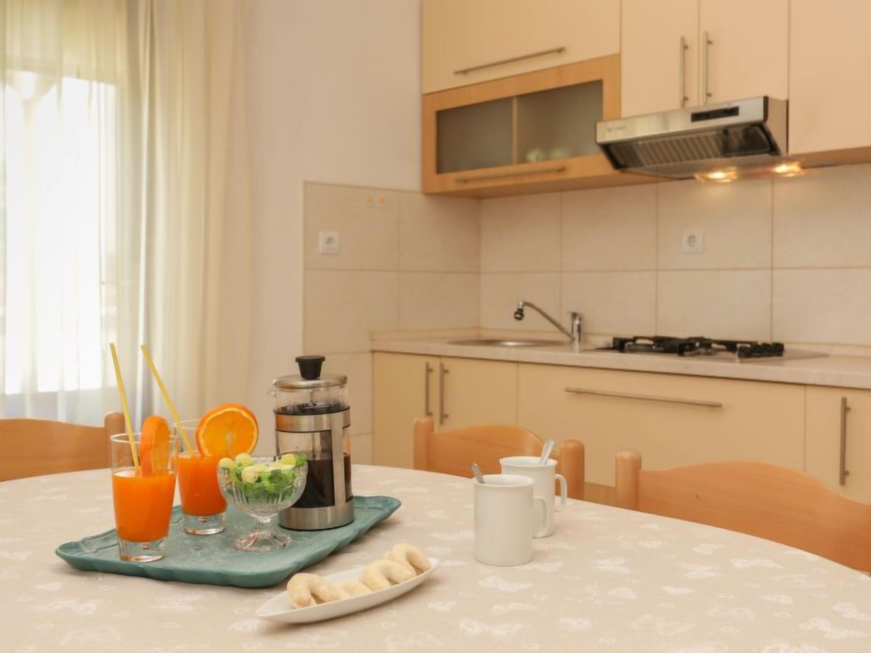Une cuisine avec une table mise pour le petit-déjeuner, comprenant du jus d’orange, un panier de fruits et une carafe.