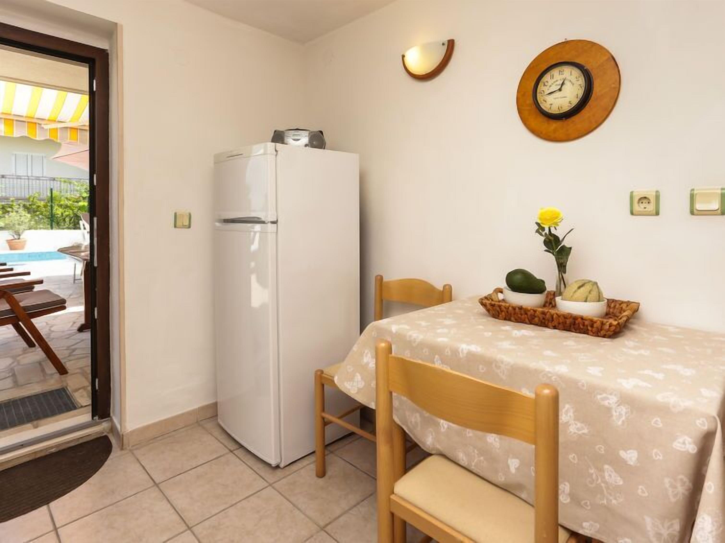 A compact kitchen with a white refrigerator, a dining table with a floral tablecloth, and a wall clock.