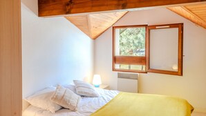 Quarto com cama, mesa de cabeceira, luminária, janela com vista para árvores e teto de madeira.