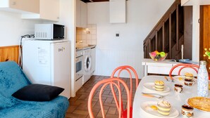 Uma cozinha compacta com micro-ondas, forno e máquina de lavar. Há uma mesa de jantar posta com pratos, copos e um bolo.