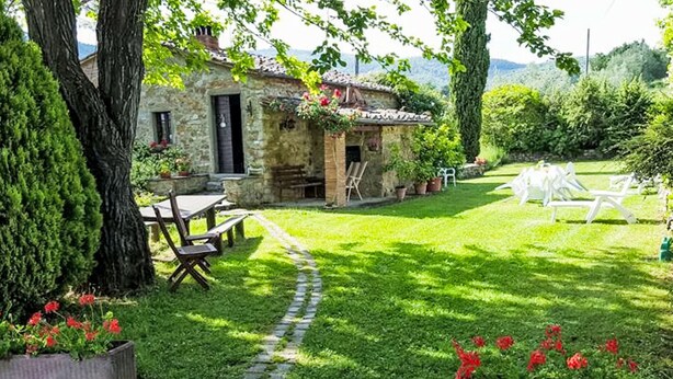 Uma casa de pedra com um caminho de jardim, área de estar ao ar livre e vasos de plantas.