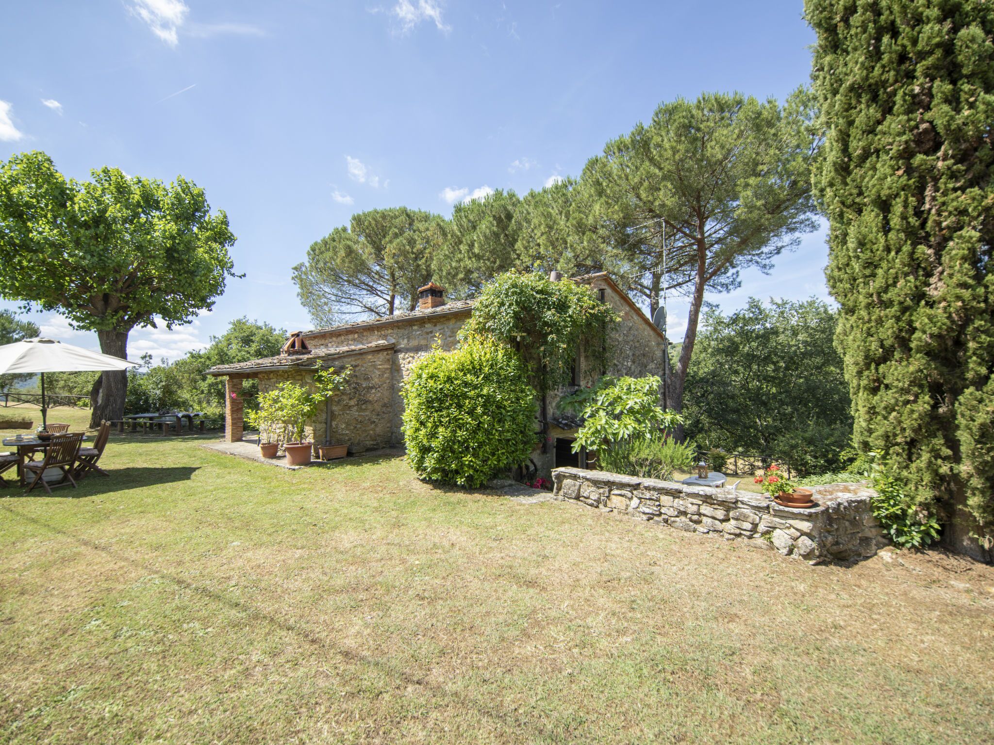 A rustic stone house with a garden, outdoor seating, and a large tree.