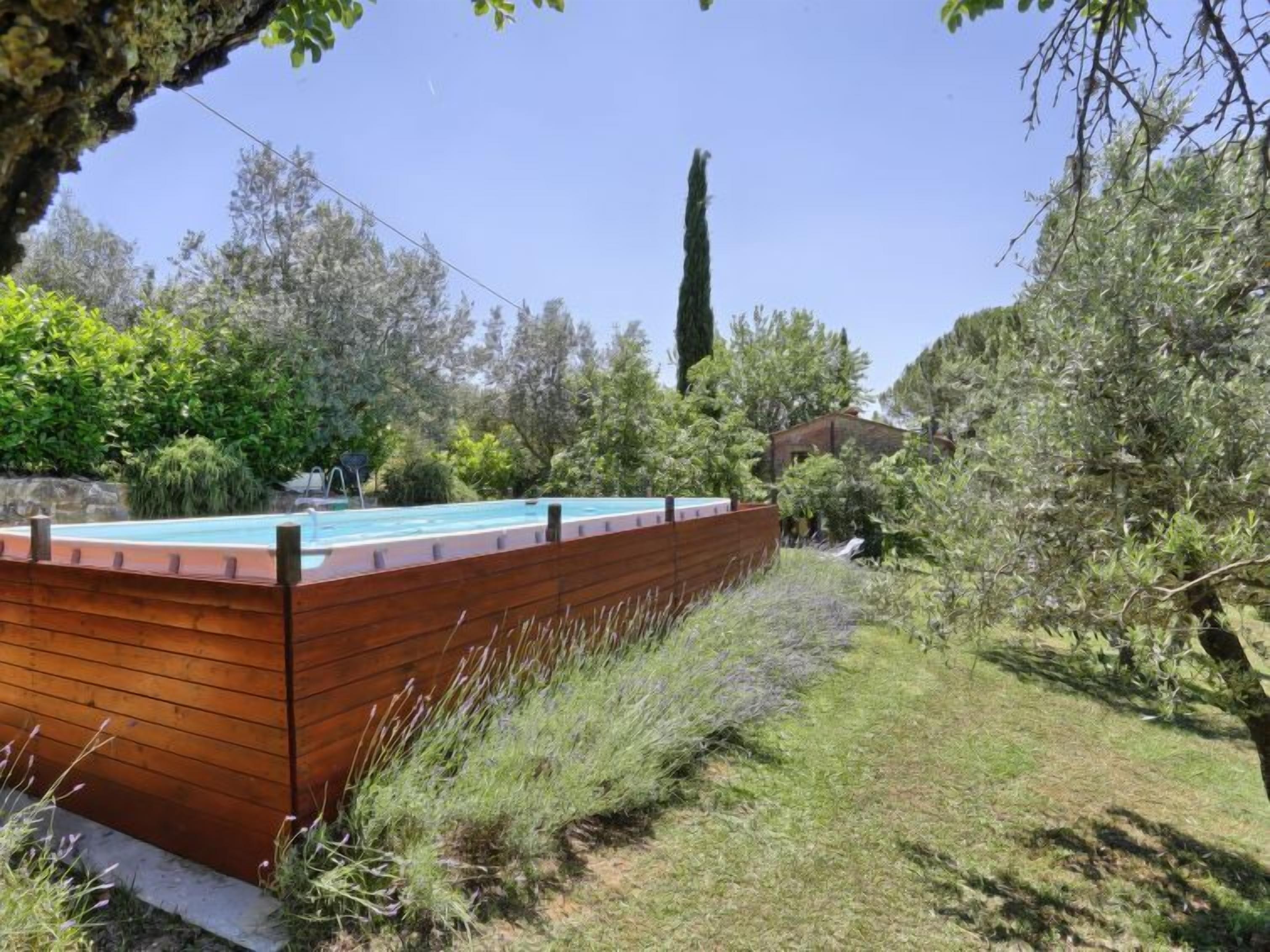 A swimming pool with a wooden deck, surrounded by lush greenery and trees.