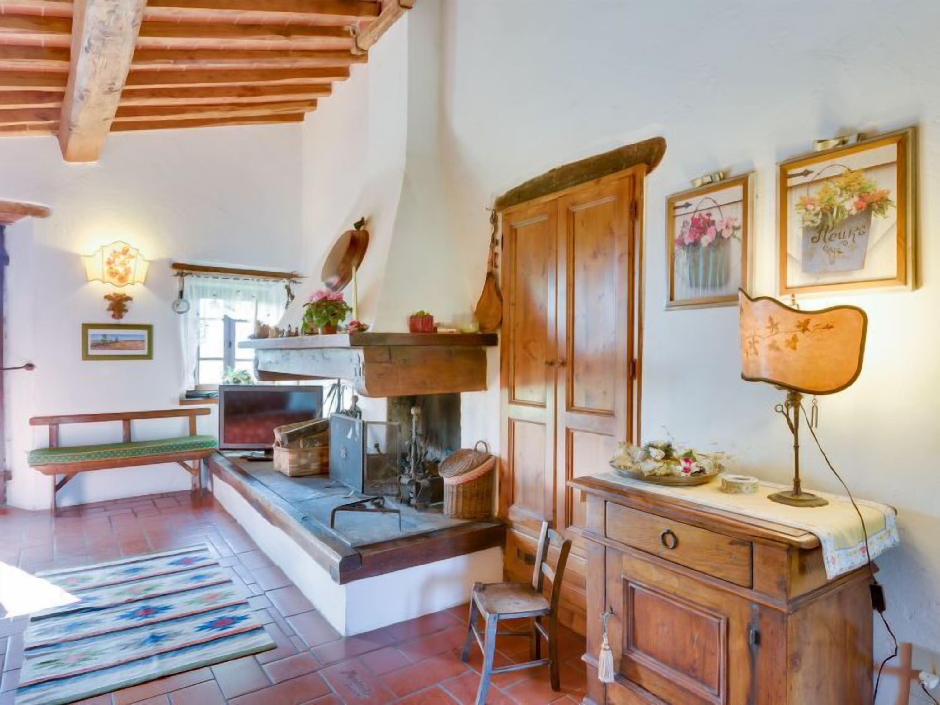 A rustic kitchen with wooden beams, a bench, a fireplace, and a wooden cabinet.