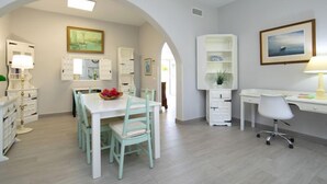 A bright, open-plan living area with a dining table, chairs, and a desk with a computer. There are white cabinets, a lamp, and artwork on the walls. - Vacation home Alan by Interhome (Albir)