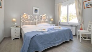 A bedroom with a bed, bedside tables, a chair, a window with curtains, and a radiator. - Vacation home Alan by Interhome (Albir)