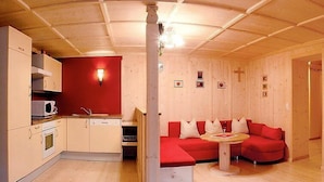 Une pièce compacte comprenant un coin cuisine, un canapé rouge et une petite table à manger.