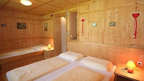 Une chambre de style cabane en bois, avec deux lits simples, une petite table avec une lampe et des décorations en forme de cœur sur les murs.