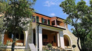 Una casa a due piani con facciata in pietra, ampie finestre e un balcone.