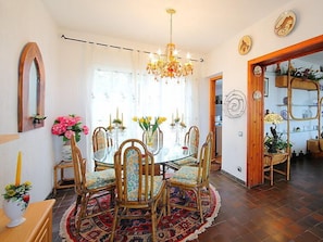 A dining area with a round glass table, six chairs, a chandelier, and a patterned rug.