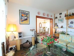 A living room with a sofa, a glass coffee table with a vase of flowers, a lamp, and a painting on the wall.