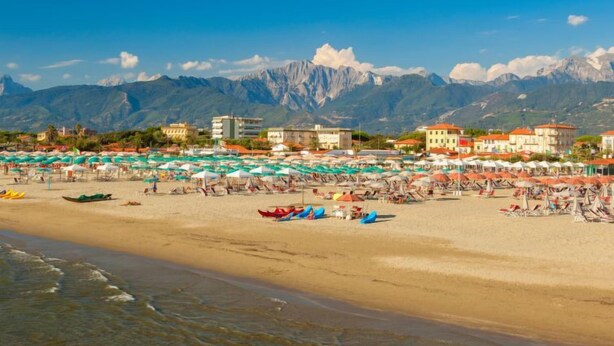 A beach with umbrellas and boats, buildings in the background, and mountains. - Antonia by Interhome (Marina Pietrasanta)